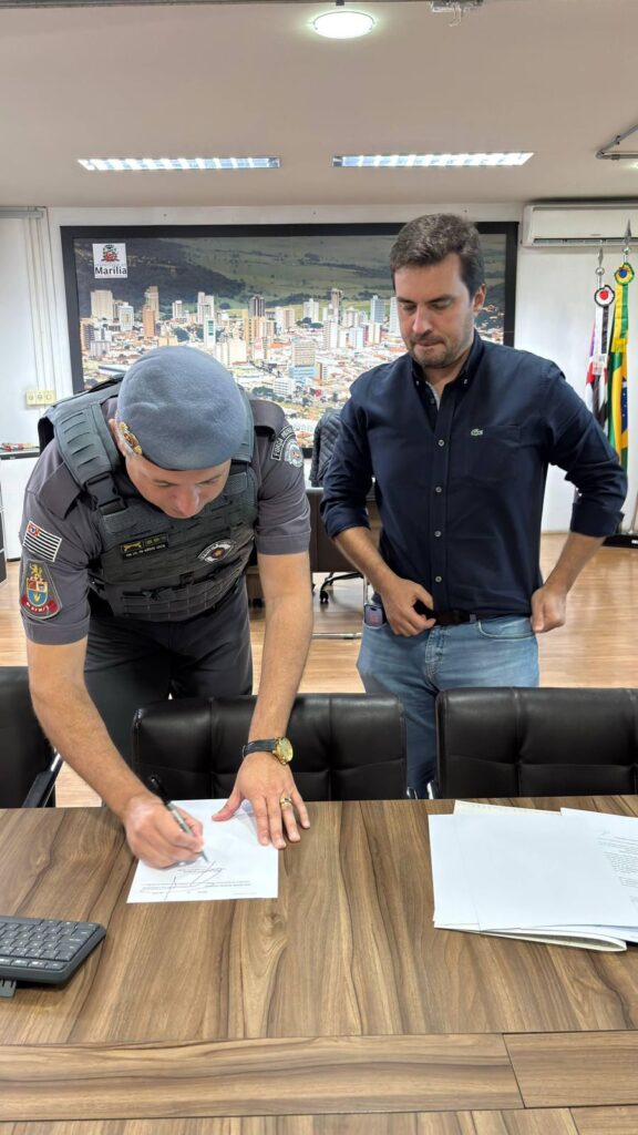 Coronel Costa assina convênio, sendo observado por Viniciuis - Colab./Ass. de Imprensa